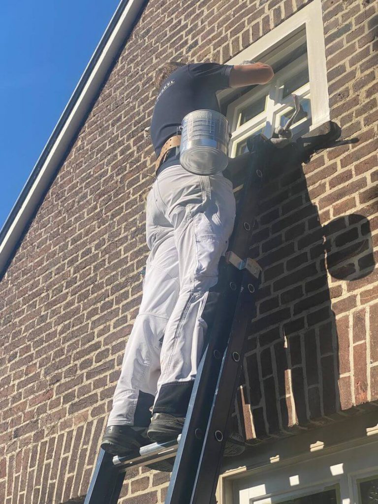 Schilder schildert veilig op een ladder aan een kozijn met een verfhouder | Paintholder