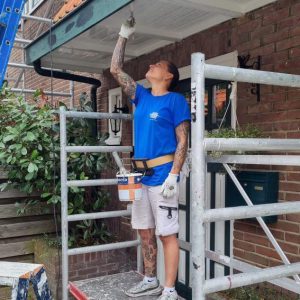 Schilder schildert veilig met de paintholder | verfblikhouder op een steiger aan de boeiplanken