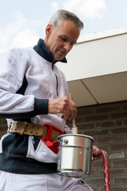 Schilder staat veilig op een trap te schilderen door middel van de Paintholder die die om heeft