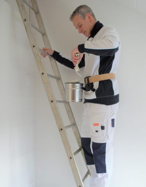 Schilder werkt veilig op een ladder door gebruik te maken van de Paintholder. Hij kan zich nu met één hand vast houden aan de ladder